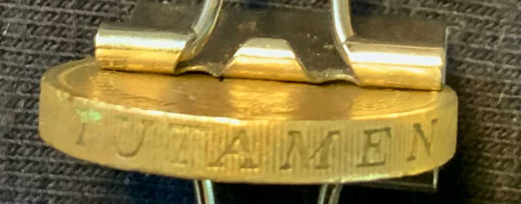 photo of the rim of a British pound coin, with milling and Latin word "tutamen" or protection in bold letters